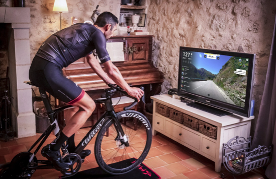 Homme pédalant sur un vélo d'intérieur avec un parcours virtuel à la TV